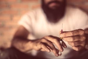 Man with beard holding syringe with heroin inside