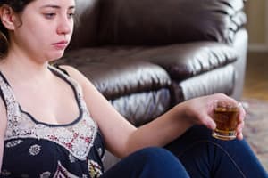 Mujer sentada frente al sofá sosteniendo un disparo de alcohol pensando en la salud reproductiva