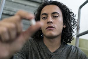man with addiction holds out pill in front of his face contemplating