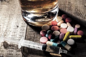 steroid pills and needles next to a glass of alcohol