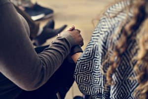 Primer plano de dos mujeres sentadas en sillas tomados de la mano en el grupo de apoyo de alcoholismo