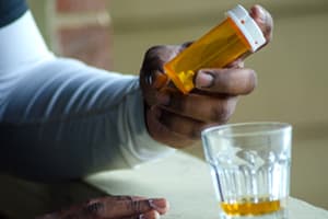 Addictive Potential of Xanax Man holding xanax pill bottle with glass of alcohol on table in front of him
