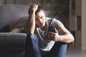 Help for Drug Abuse man portraying an addict in distress sitting on floor looking at phone seeking help for drug abuse