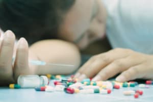 Librium Overdose woman passed out on floor holding needle in front of librium pills portraying overdose dangers when mixing drugs