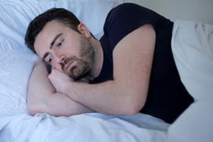 Sad man trying to sleep on his side, concept of insomnia