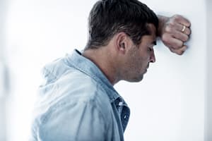 Man dependent on butalbital leans against wall stressed